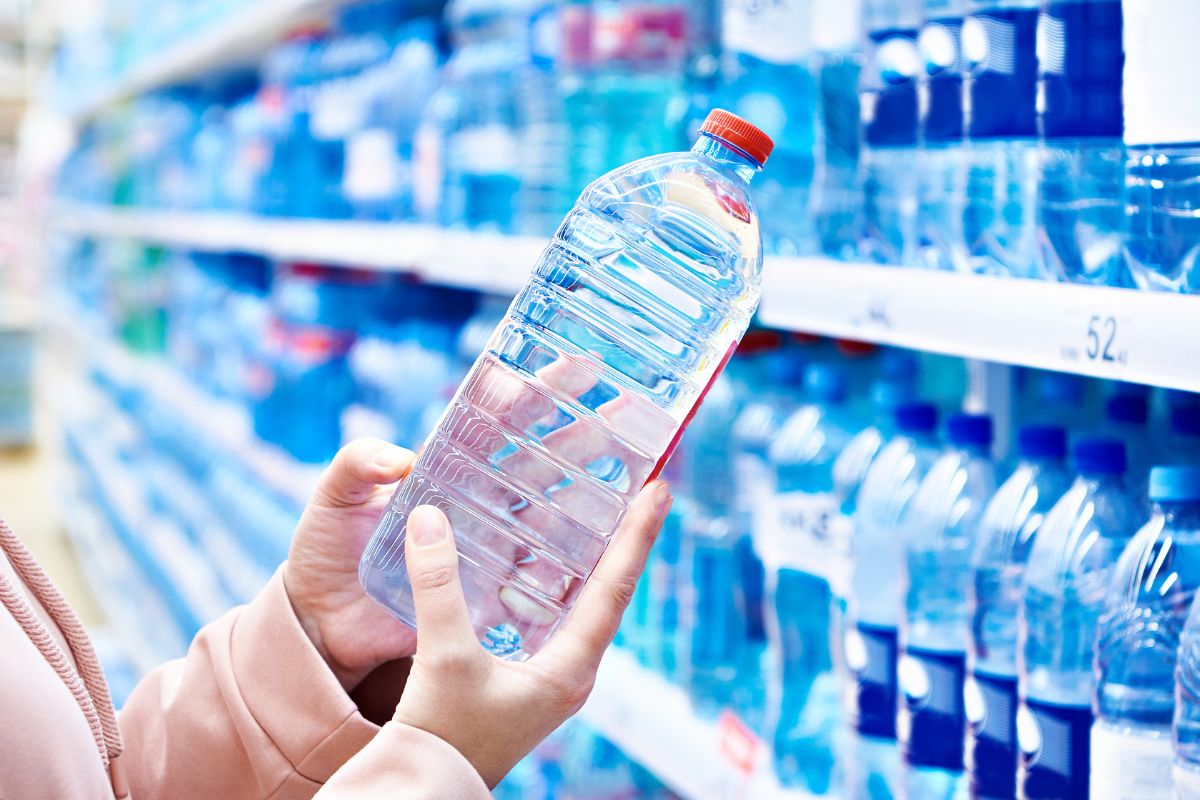 The picture tells about a girl's hand picking up a water bottle in a store which refers to fancy bottled water Adding up fastm carrying a reusable bottle can save money and reduce waste.