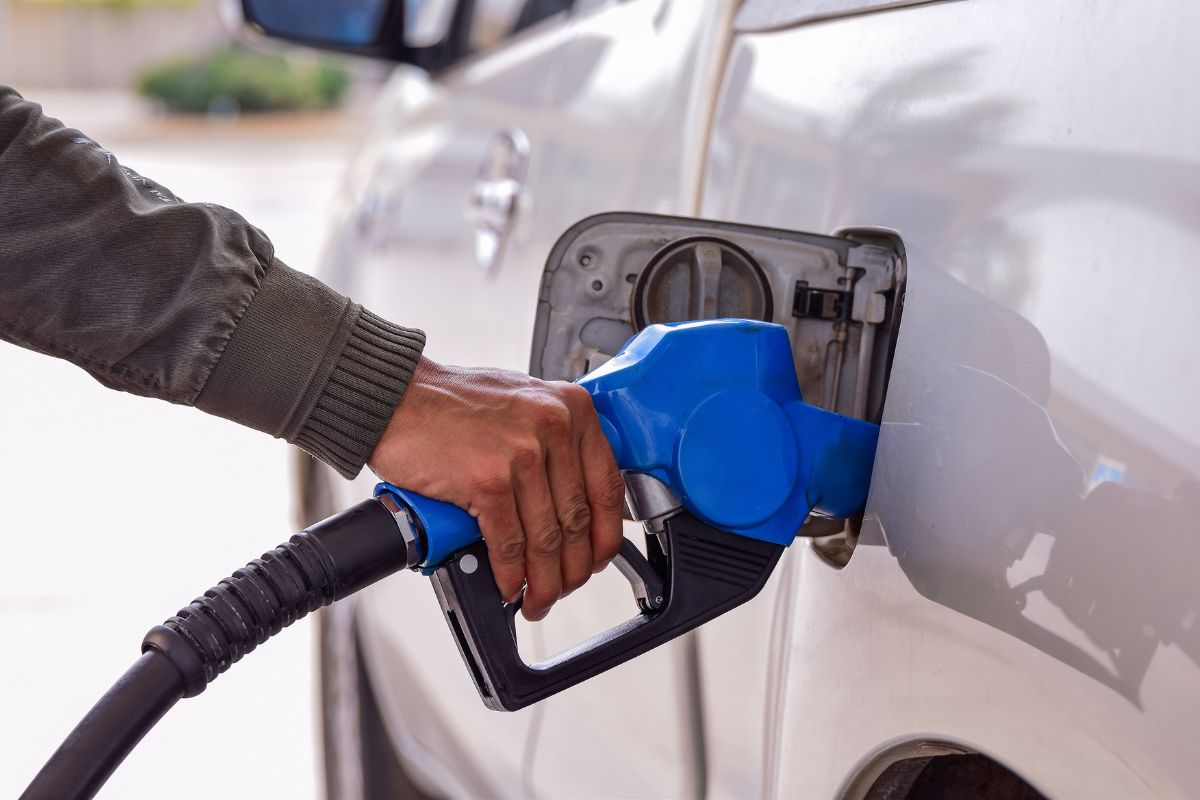 The image tells about a man's hand refilling fuel on his car which means premium fuel when not needed pay extra for it, checking your car's requirements can help cut unnecessary expenses.