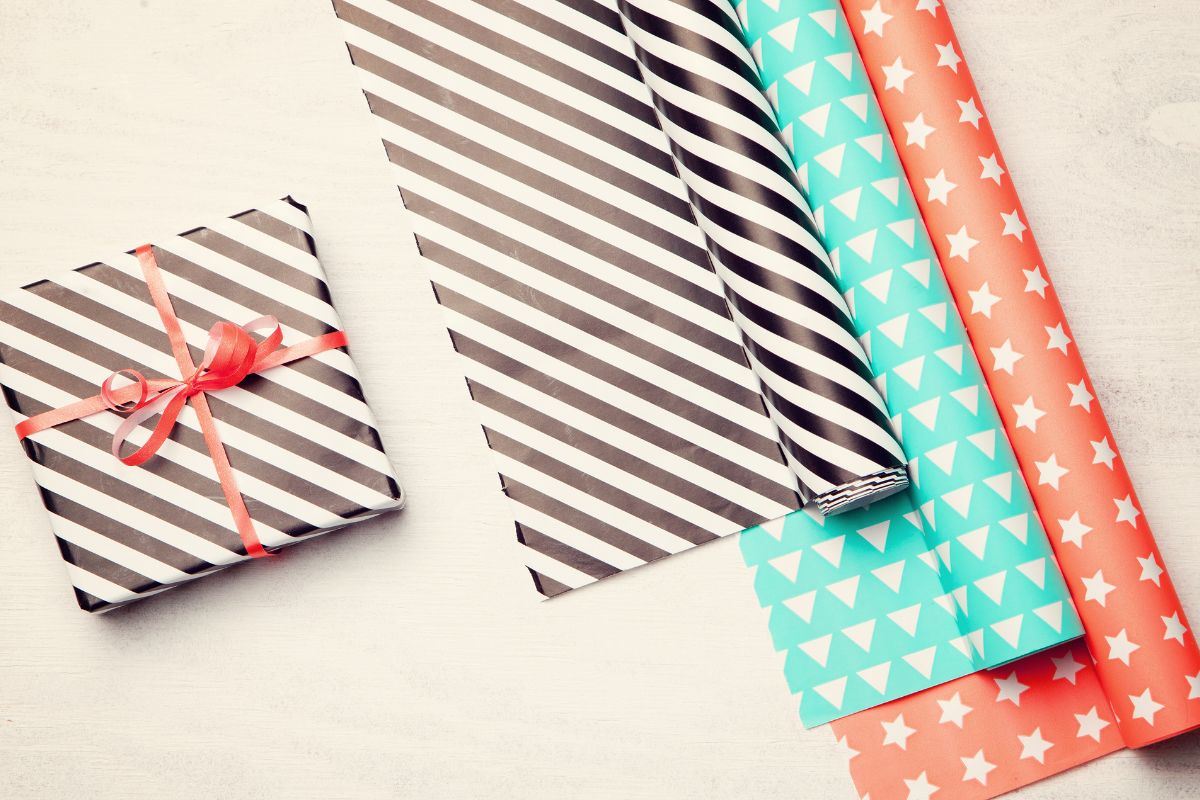 The picture shows a gift box and wrappers on the table indicating that excessive gift wrapping supplies can be surprisingly expensive, reusing wrapping paper can save and reduce waste.