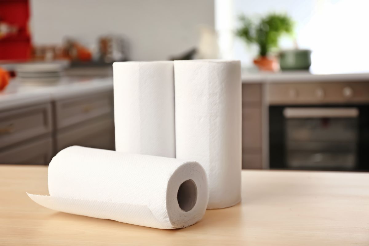 The image shows paper towels on the table which means paying for name-brand household staples that are overpriced, switching to store-brand products can save significant amounts without sacrificing effectiveness.