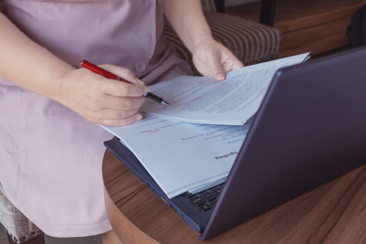 The photo shows a laptop and a girl's hand checking the papers indicating that proofreading and editing services are a reliable way to make money online with flexible hours.