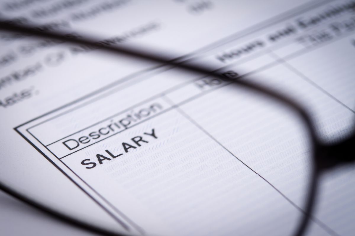 The picture shows a piece of paper with notes and an eyeglass indicating to living paycheck to paycheck without tracking expenses makes it hard to save or plan for the future.