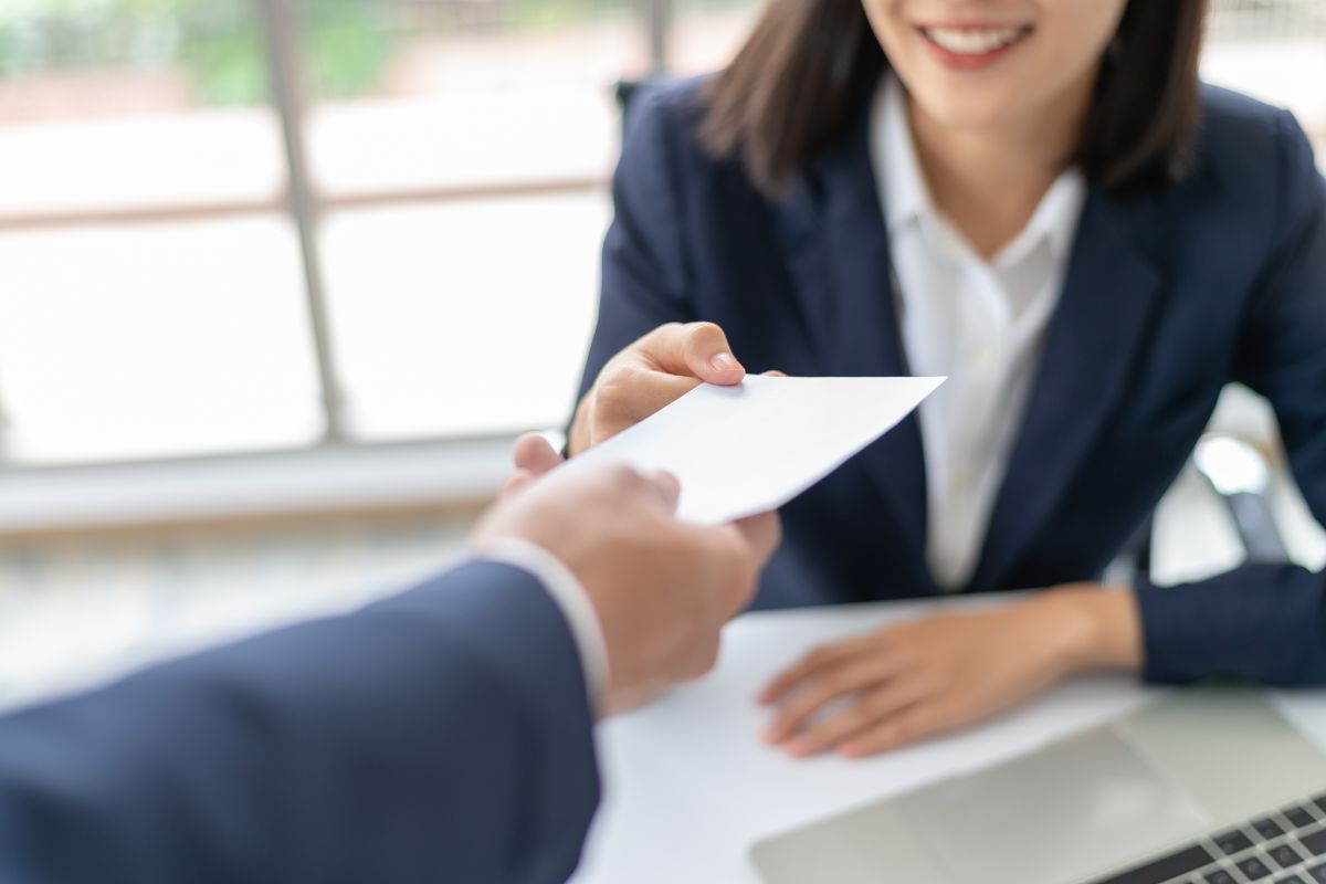 The image shows a boss's hand handing a white envelope to the girl indicating that failing to negotiate salary and benefits can leave money on the table, speaking up about earnings is key to long-term financial growth.