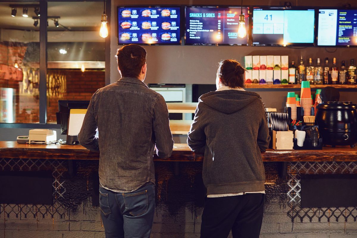 The image shows two men ordering at a fast food restaurant.