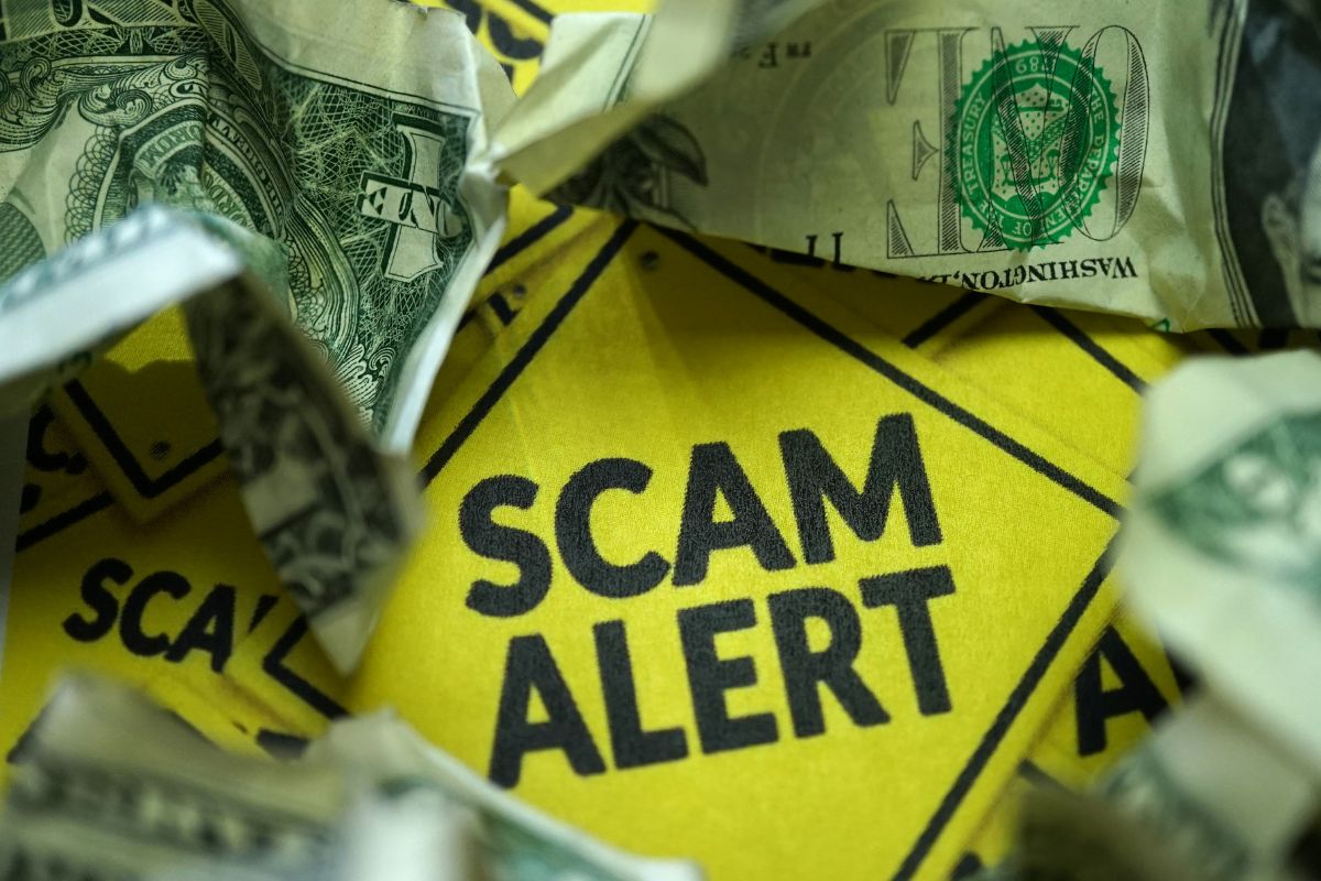 The picture is about a scam alert signage and dollar bills.