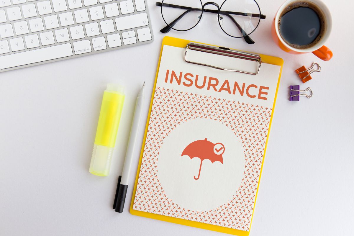 The photo tells about a keyboard, an eyeglass, a coffee, pins, a pen, a marker, and a clipboard with notes which refers to over-insuring assets and health waste money, comparing plans and adjusting coverage can save money.