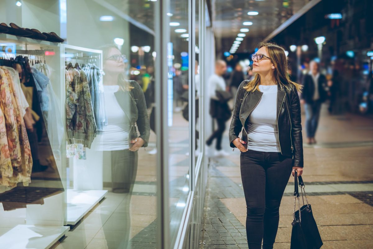 The photo shows a girl looking at the window glass of the store with clothes referring to how emotional spending leads to regret and financial strain, better habits lead to better financial choices.