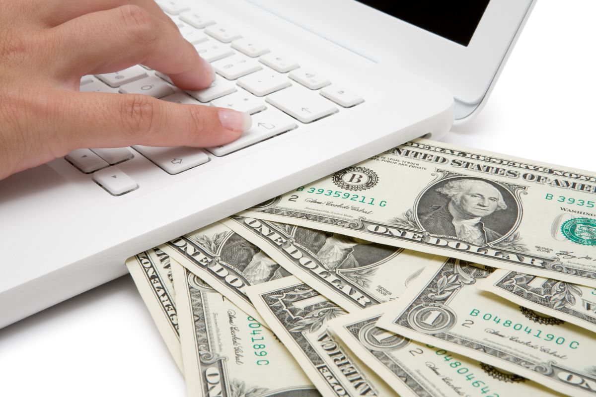 The picture shows a man's hand typing on the laptop with dollar bills which refers to ignoring side hustles opportunities can lose extra income, having multiple income sources lead to financial stability.