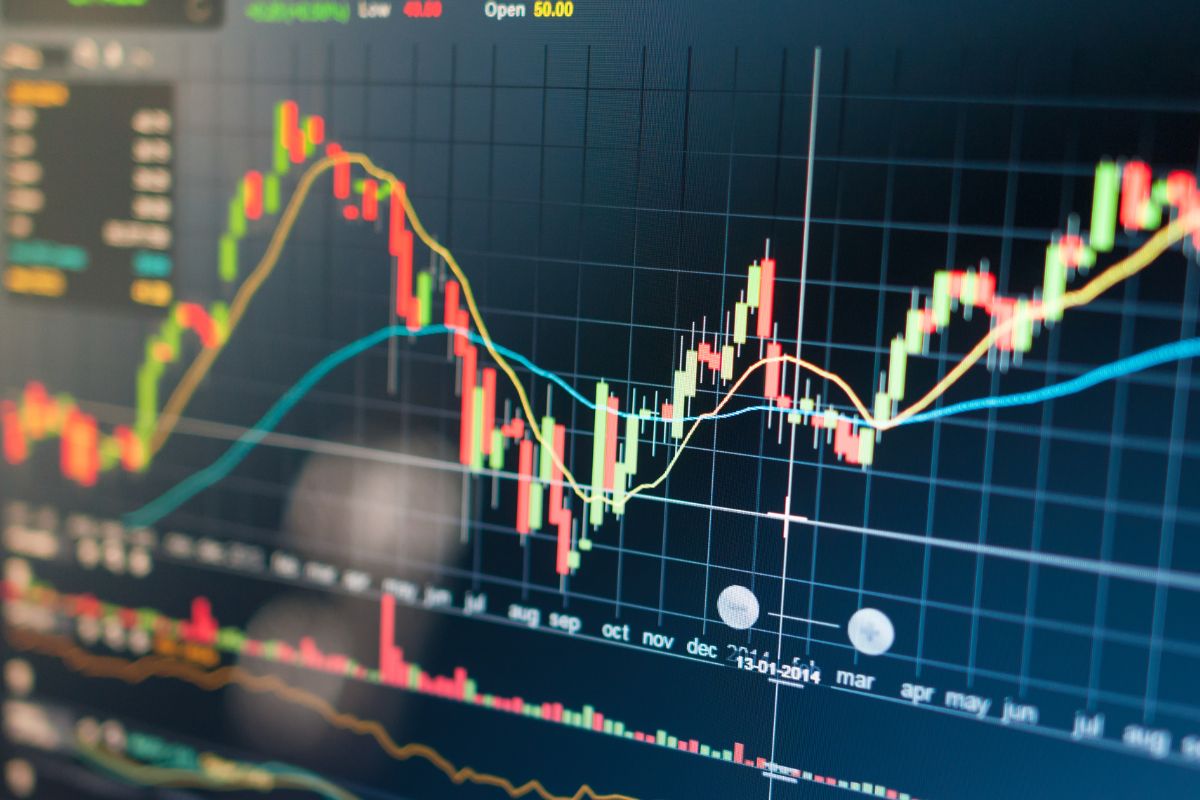 The photo shows a screen with graph displays referring to the stock market and one of Warren Buffett's quotes that wealth is built through patience.