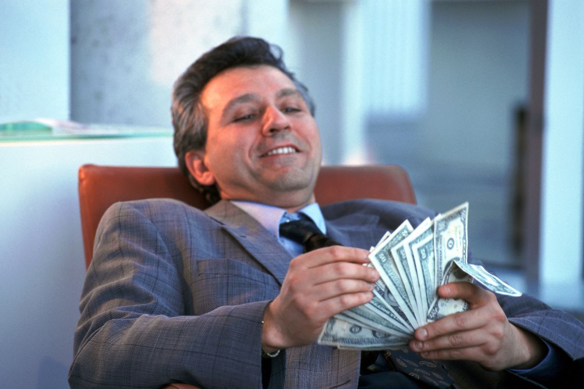 The picture tells about a man relaxing on a chair while counting dollar bills referring to making money work for you and building lasting wealth.