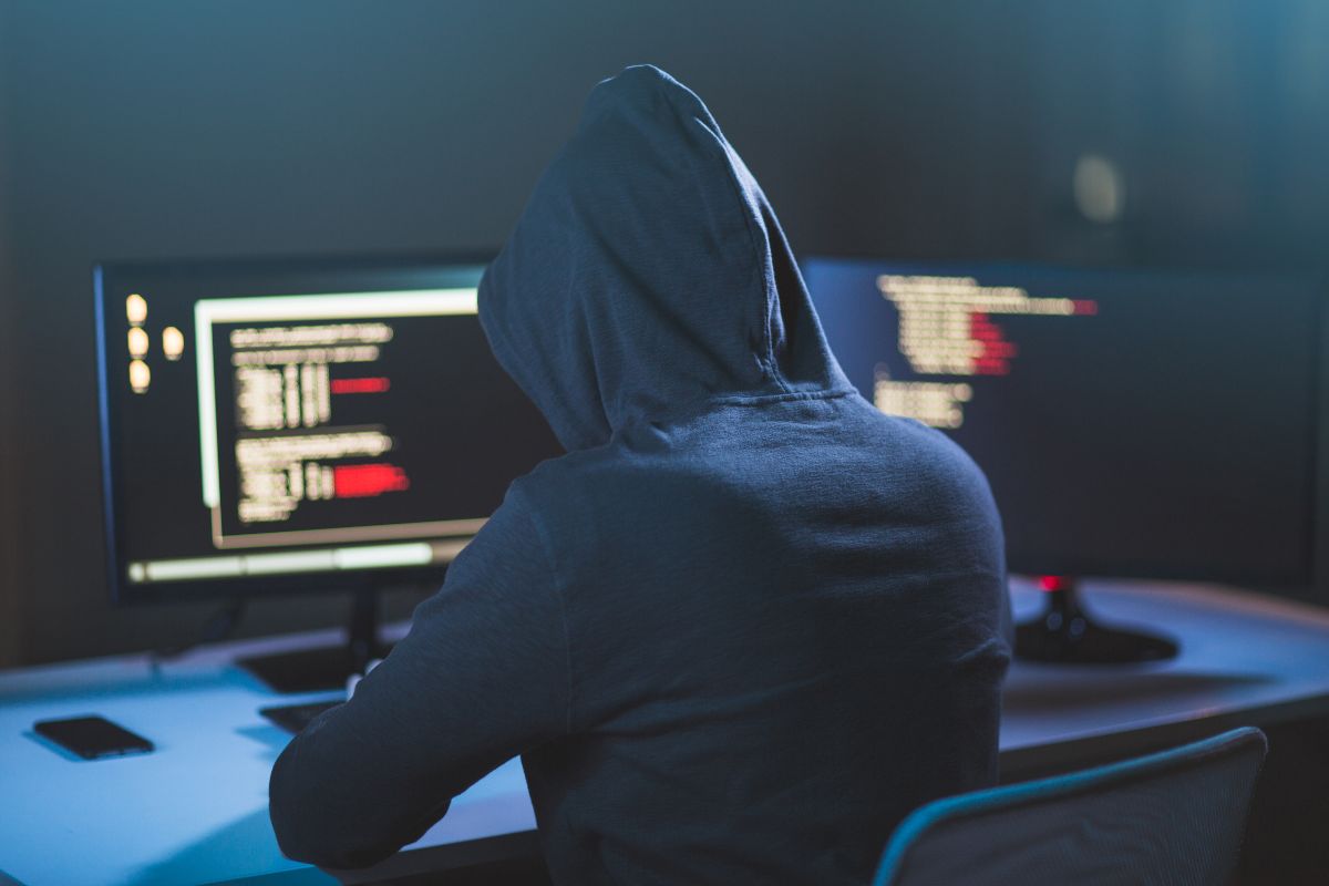 The photo of a mysterious man in a jacket using a computer with a screen display indicates that an ethical hacker testing company security systems is one of the profitable careers that allows one to set own rates.