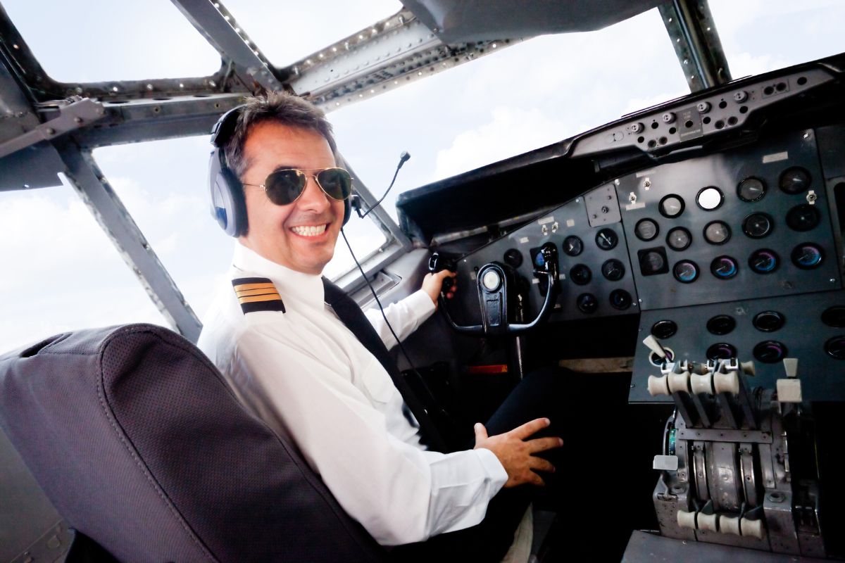 The image tells about a man in a white uniform inside a plane referring to a commercial pilot that comes with great pay and benefits and strong job security.