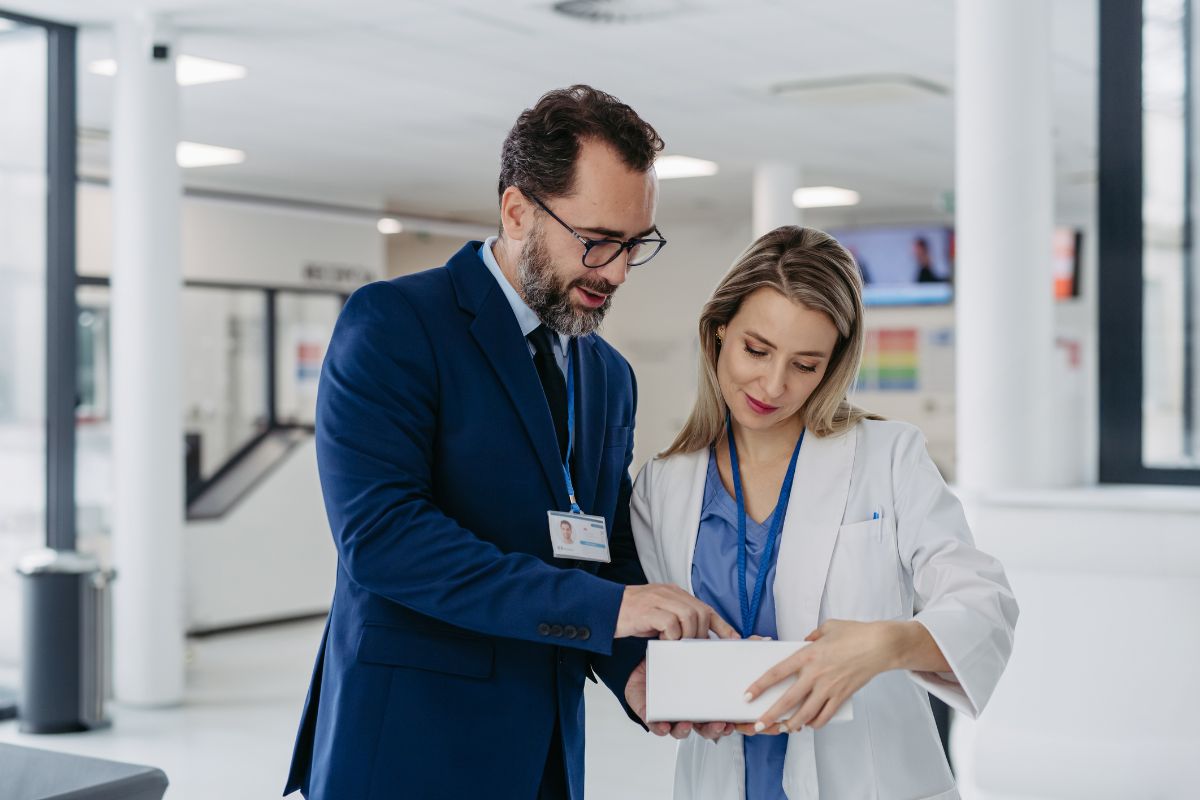 The photo tells about a man in a suit telling the girl in a white suit about the thing on a white box which refers to a pharmaceutical sales representative who sells medicine to doctors and hospitals that pays well and is very profitable.