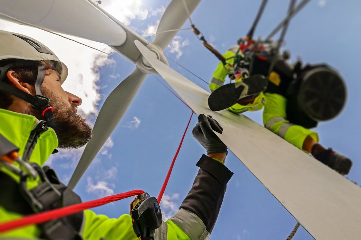 The image shows working men in their uniform which refers to wind turbine technicians who install and repair wind turbines that produce clean energy with a high-paying job.