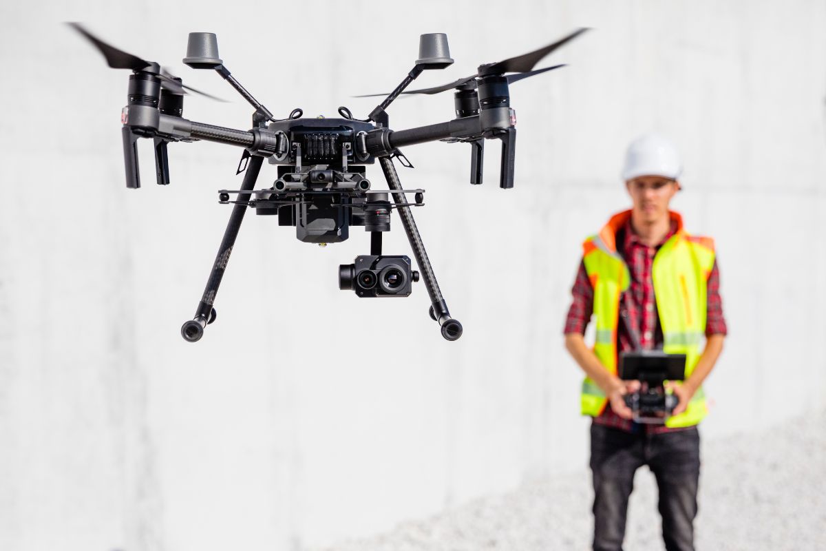 The picture shows a man holding a remote while looking at the drone referring to a drone operator for film helping businesses monitor large that charge high rates for their services.
