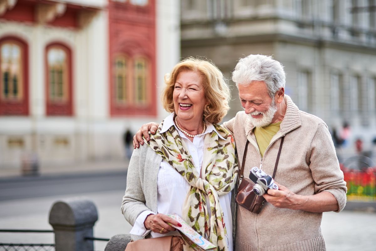 The photo shows a senior couple holding a camera and a map which means lifestyle goals help make retirement both affordable and enjoyable.