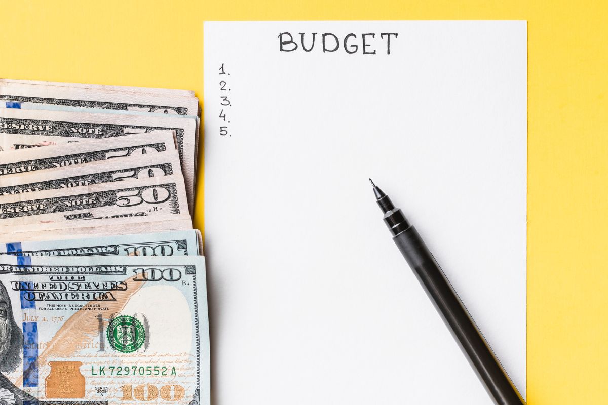 The picture shows dollar bills, a pen, and a piece of paper with notes which refers to zero-based budgeting helps track where every dollar goes and cuts unnecessary spending.