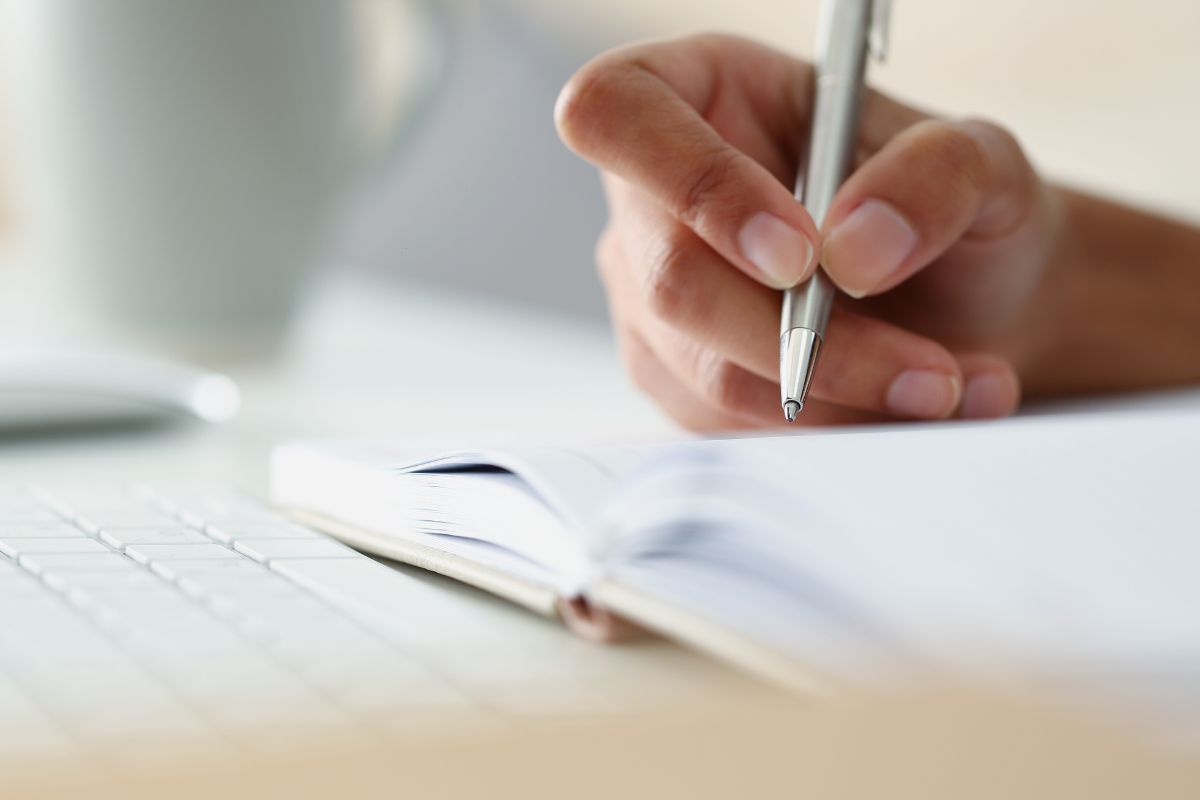 The picture shows a keyboard and a girl's hand and writing on the notebook indicating that Kakeibo is a traditional Japanese way to budget money that helps cut waste and save money fast.