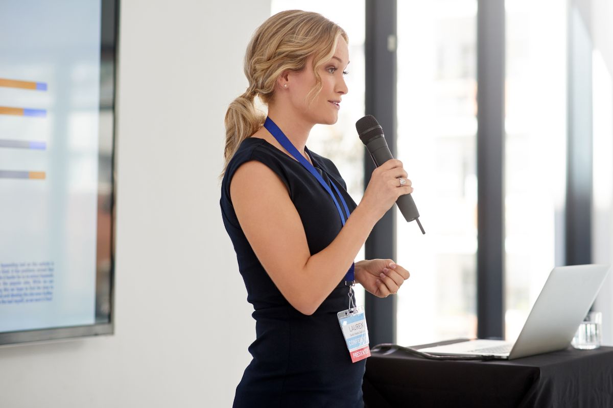 The image is about a laptop and a girl holding a mic and talking referring to how public speaking can lead to better job offers, leadership roles, and personal growth.
