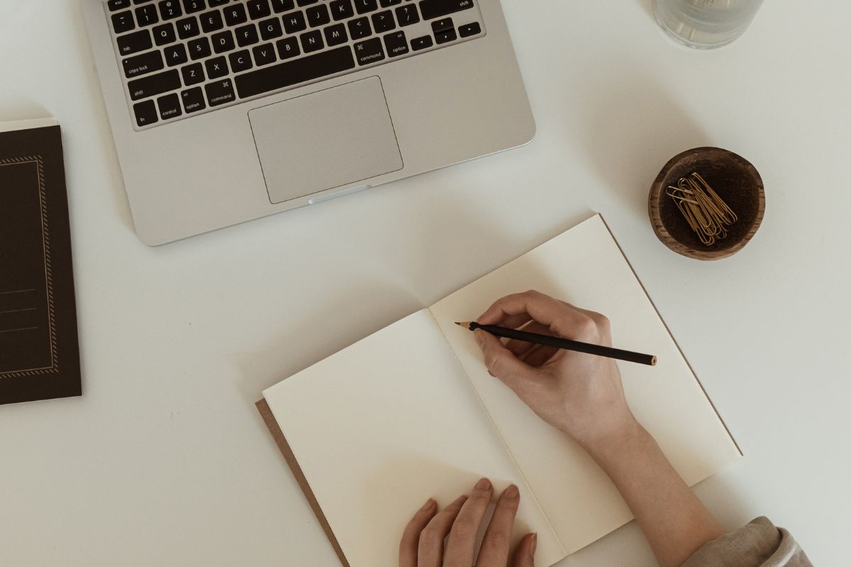 The image tells about a laptop, a bowl, and a girl's hand and writing on the notebook which means writing and storytelling opens doors in almost every career.