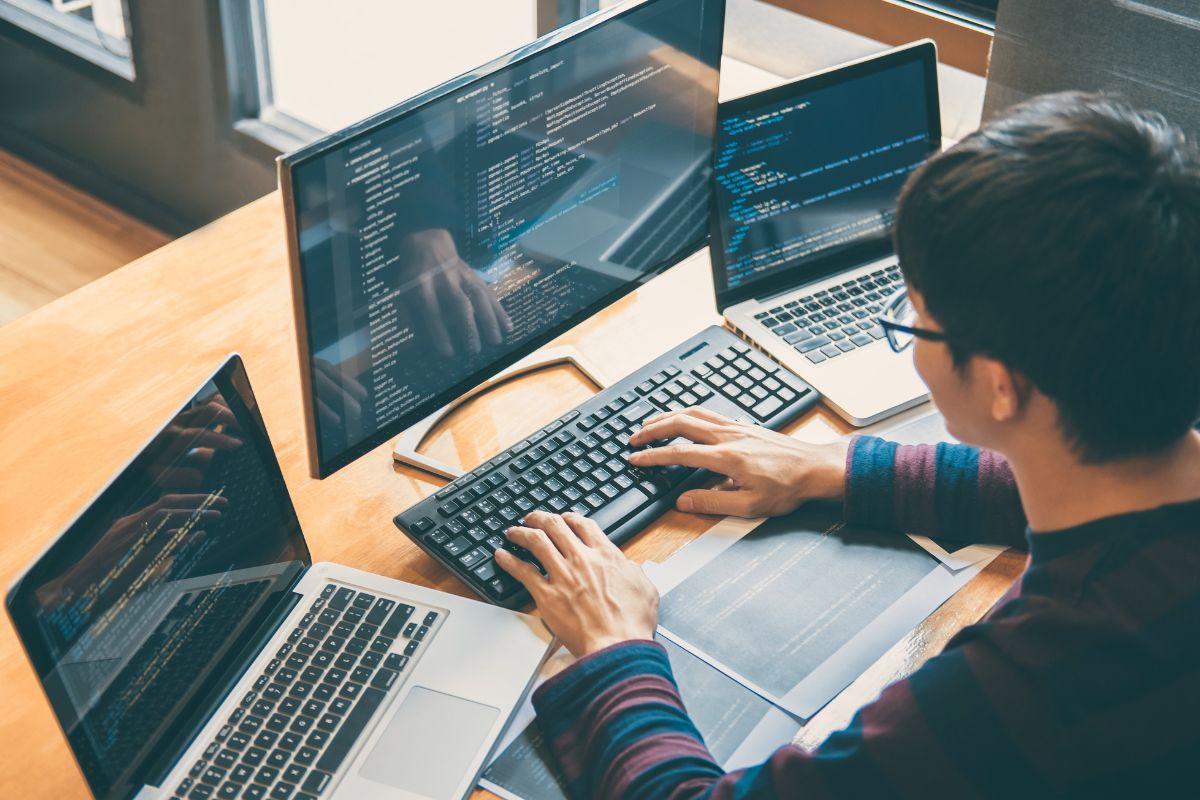 The picture tells about laptops, papers, and a young man using a computer with a screen display referring to basic coding and tech literacy makes daily tasks easier and opens up more job opportunities.