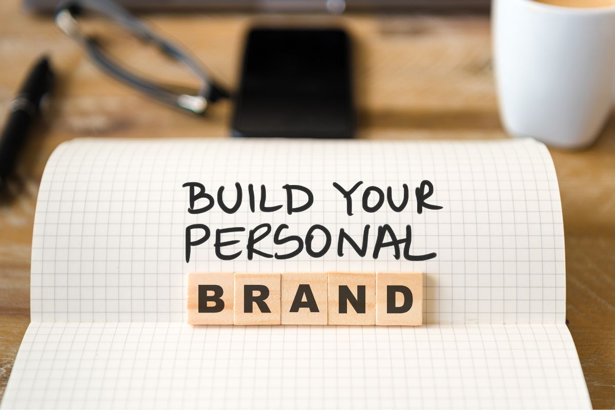 The image tells about coffee, a phone, an eyeglass, wooden cubes with letters, and a notebook with notes which means personal branding can create more career opportunities.