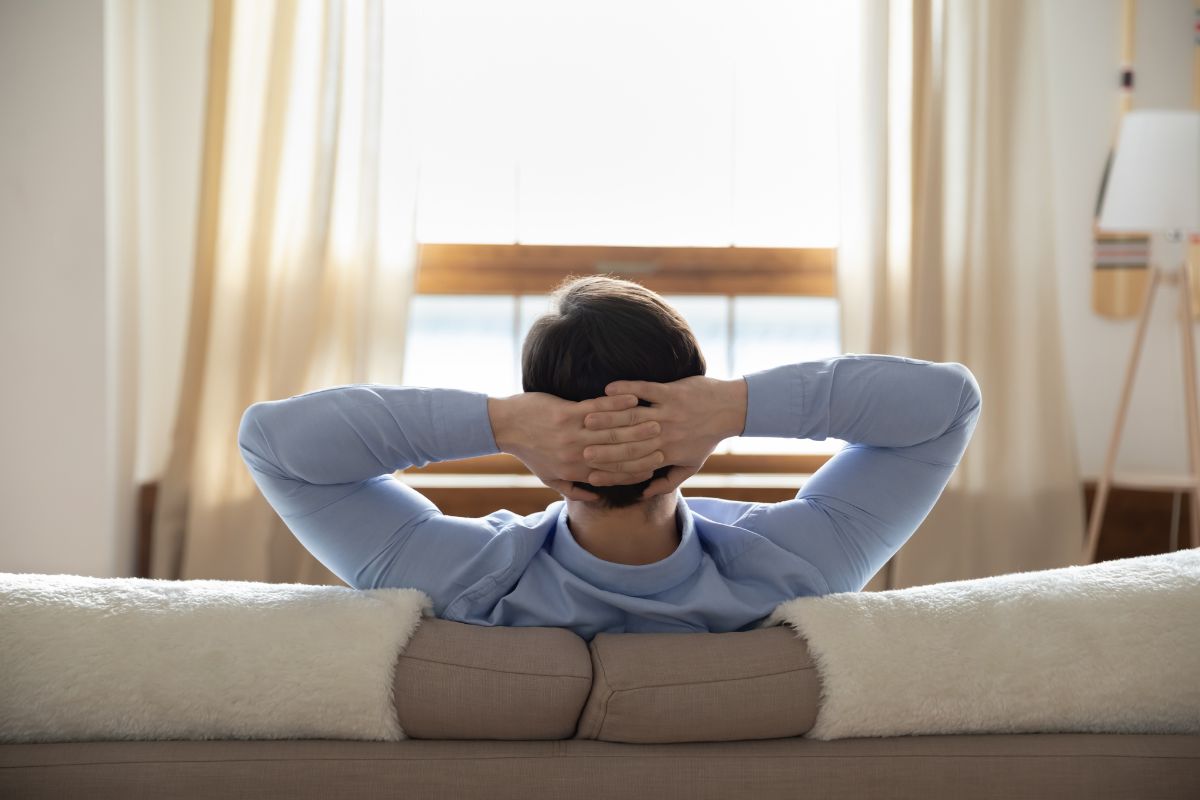 The image tells about a man sitting on the couch while relaxing referring to getting paid to housesit can a simple way to earn extra cash.