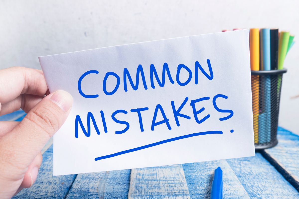 The image tells about pens and a man's hand holding a piece of paper with notes referring to common financial mistakes to avoid can help you stay financially stable.