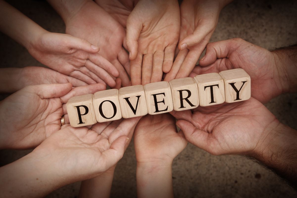 The image tells about joined hands together holding wooden cubes with letters which refers to not living in poverty by saving now helps protect your future self from financial hardship.