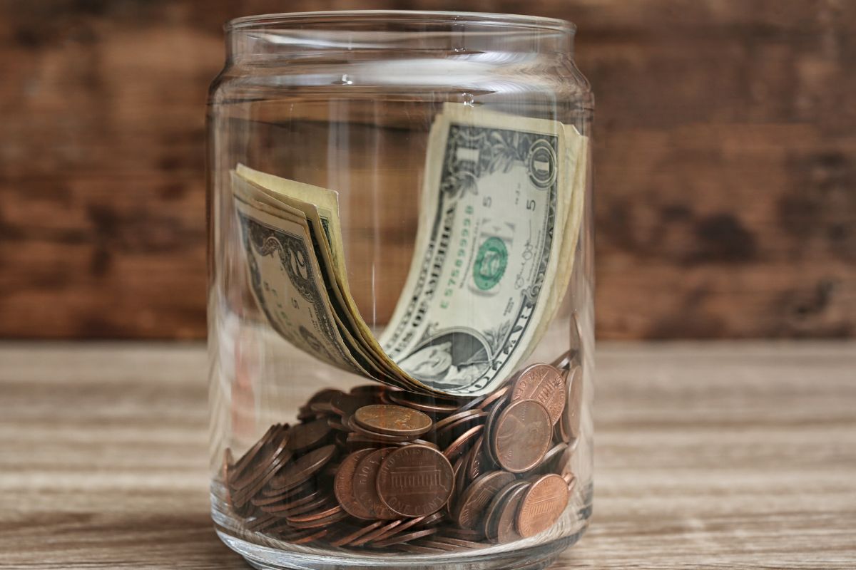 The picture shows a jar filled with dollar bills and coins.
