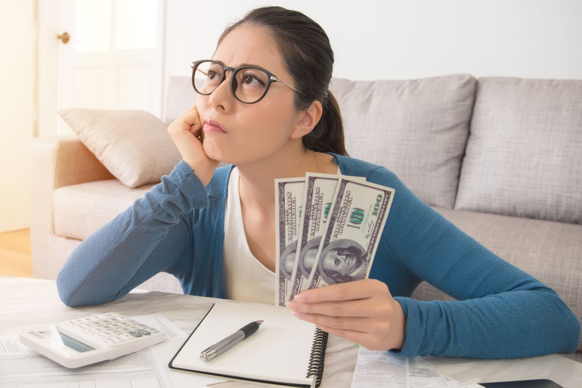 The photo a lady holding dollar bills while thinking.