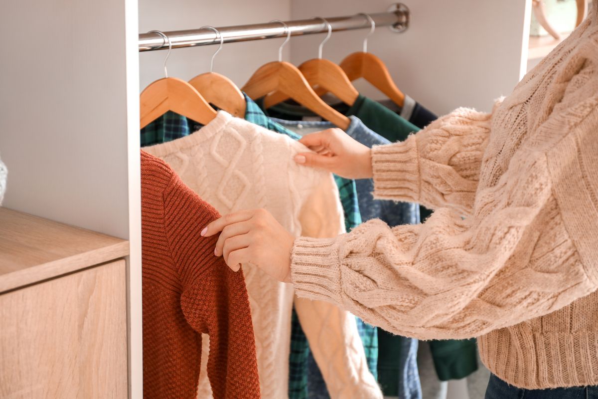 The image shows a girl choosing clothes from her wardrobe referring to doing a no-new clothes challenge as a simple way to cut back on spending and rethink shopping habits.