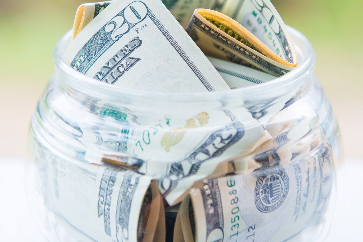 The image tells about a jar filled with dollar bills which refers to saving $1000 in a month helps you build discipline and create a strong habit of putting money aside regularly.