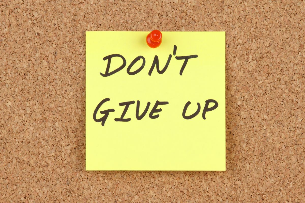 The image shows a piece of paper with notes pinned on the wall referring to not giving up and having a solid plan that helps avoid financial stress and unexpected problems.