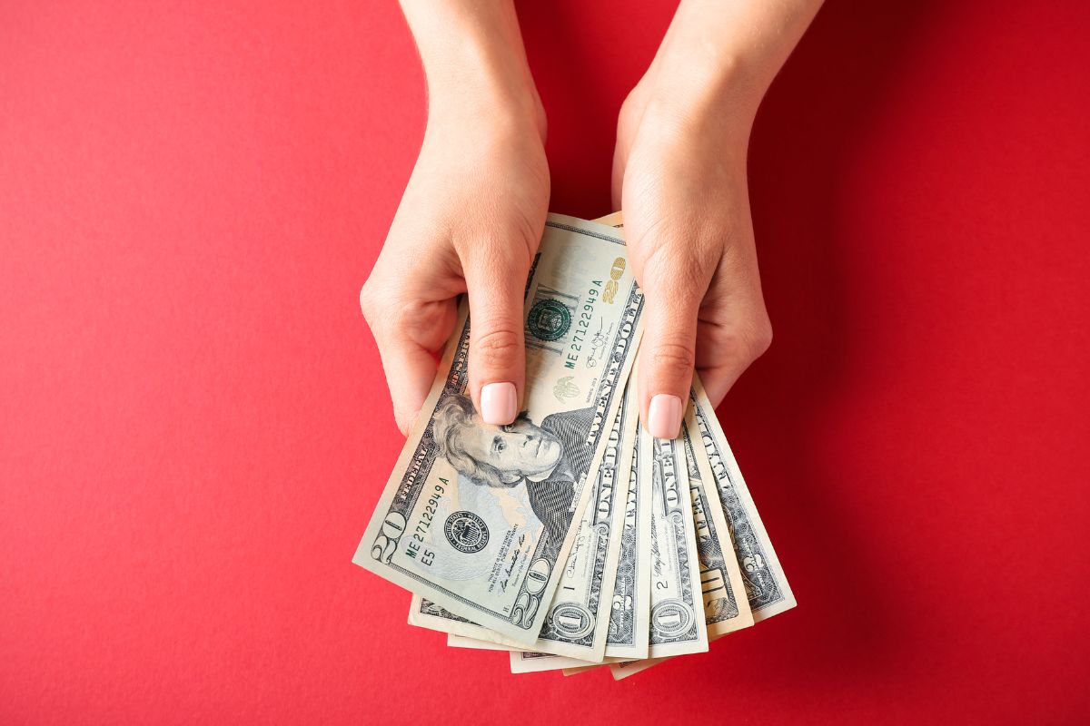 The image shows a lady's hand holding dollar bills.