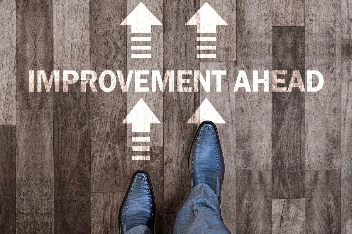 The picture of a man's foot and a wooden floor with notes and arrows referring to making small improvements daily can move you towards a life where money isn't a constant worry.