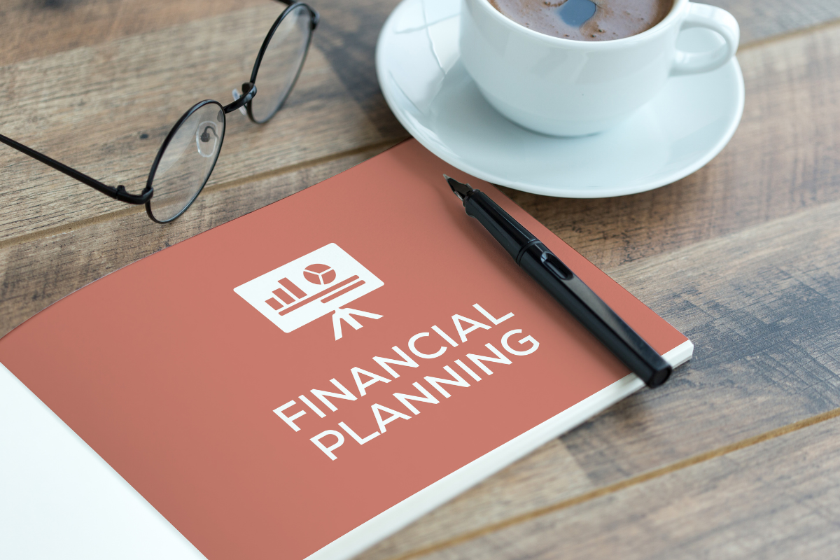 The image tells about an eyeglass, a coffee, a pen, and a book with notes referring to the definition of financial planning which helps you manage money wisely so you can meet goals and avoid stress.