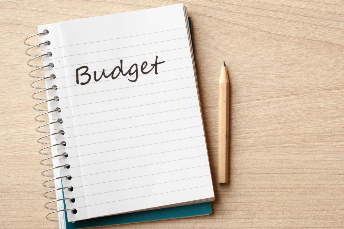 The picture shows a pen and a notebook with a note which means to create a budget that works gives you financial stability and helps avoid debt.

