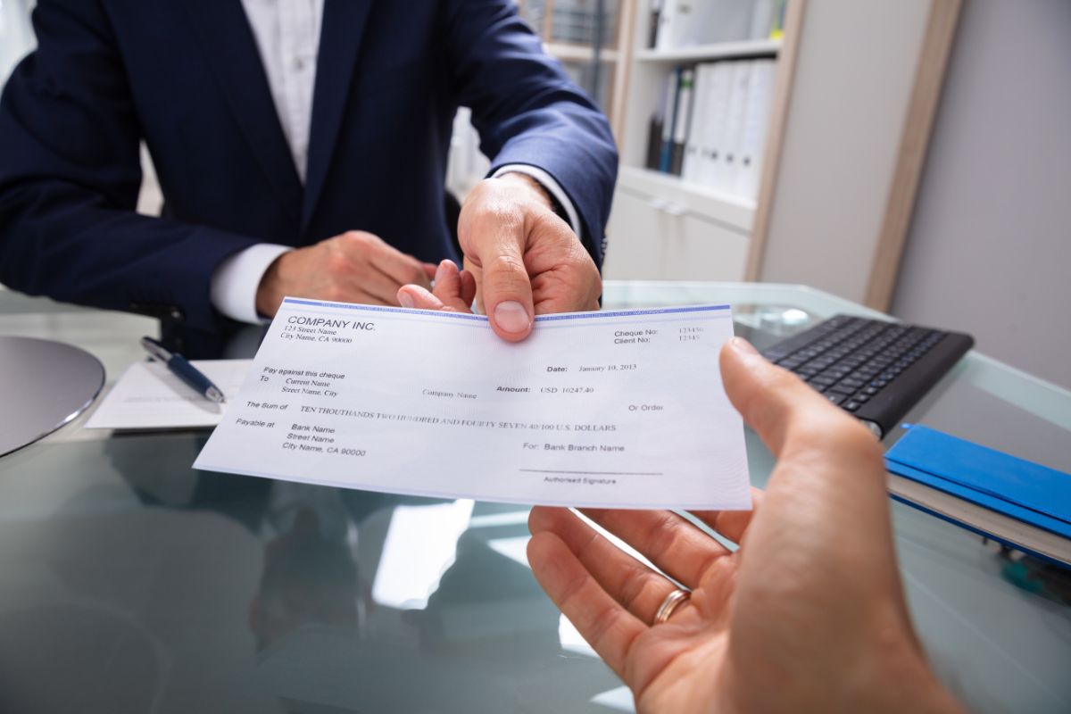 The image tells about a notebook, a keyboard, a pen, a paper, and a boss hand handing a piece of paper to the man's hand referring to living paycheck to paycheck with the goal is to break the cycle so you have more control over your money.