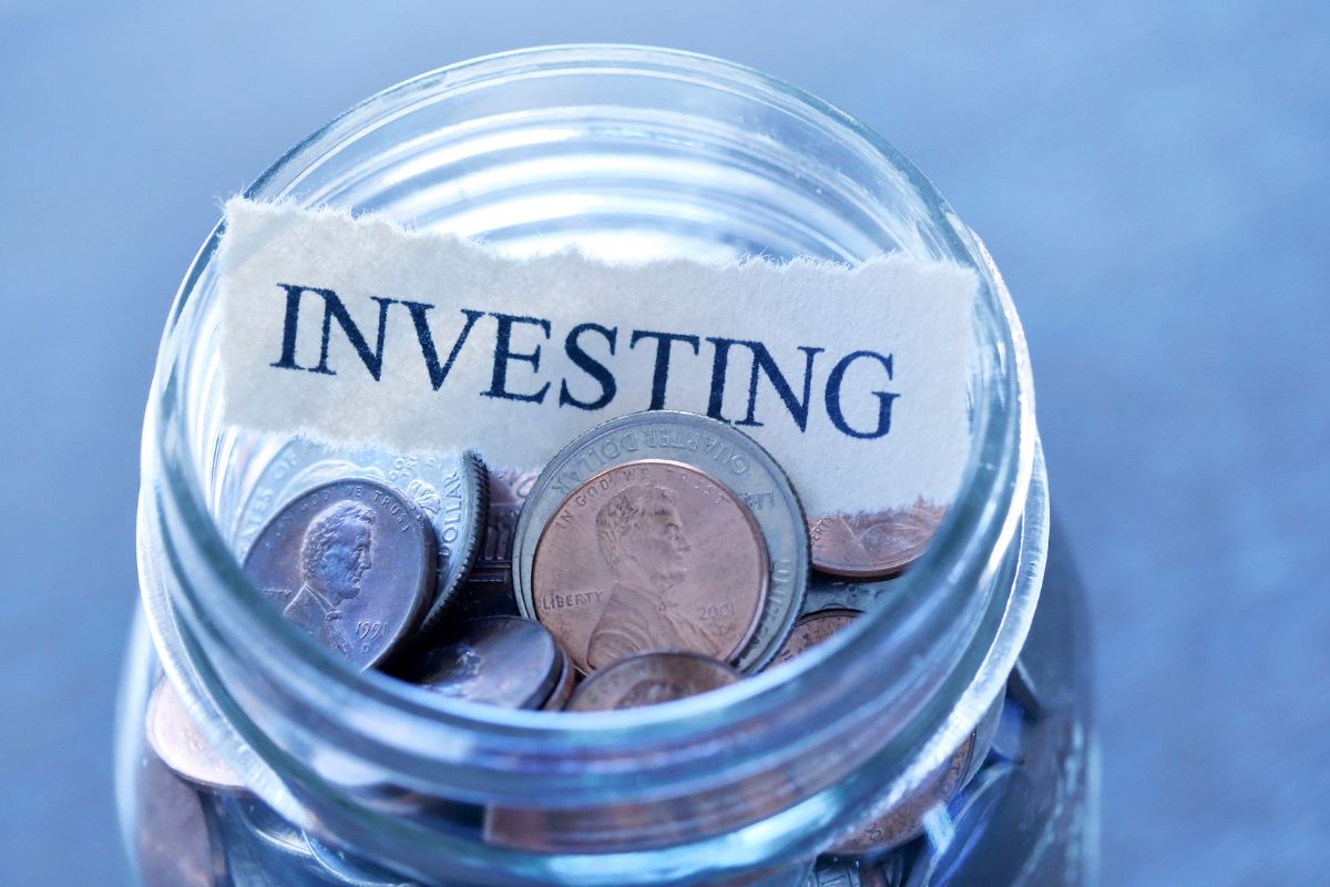 The image shows a jar filled with coins and a piece of paper with a note indicating that investing for the future helps grow your money over time.