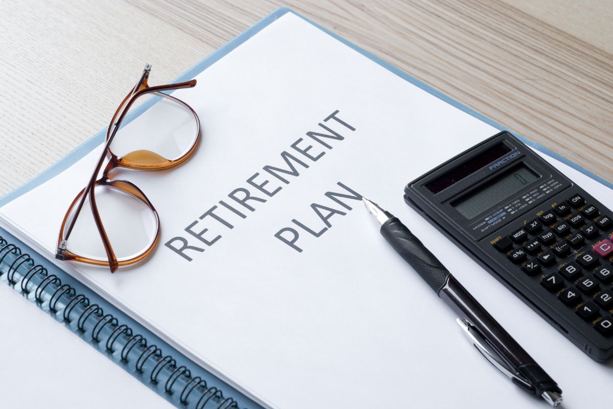 The photo shows a pen, a calculator, an eyeglass, and a notebook with notes referring to a plan for retirement to ensure financial independence in later years.
