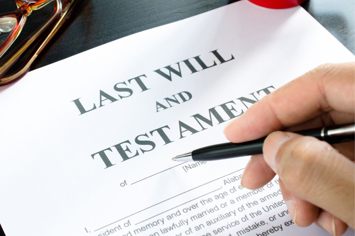 The image is about a man's hand signing a last will paper.