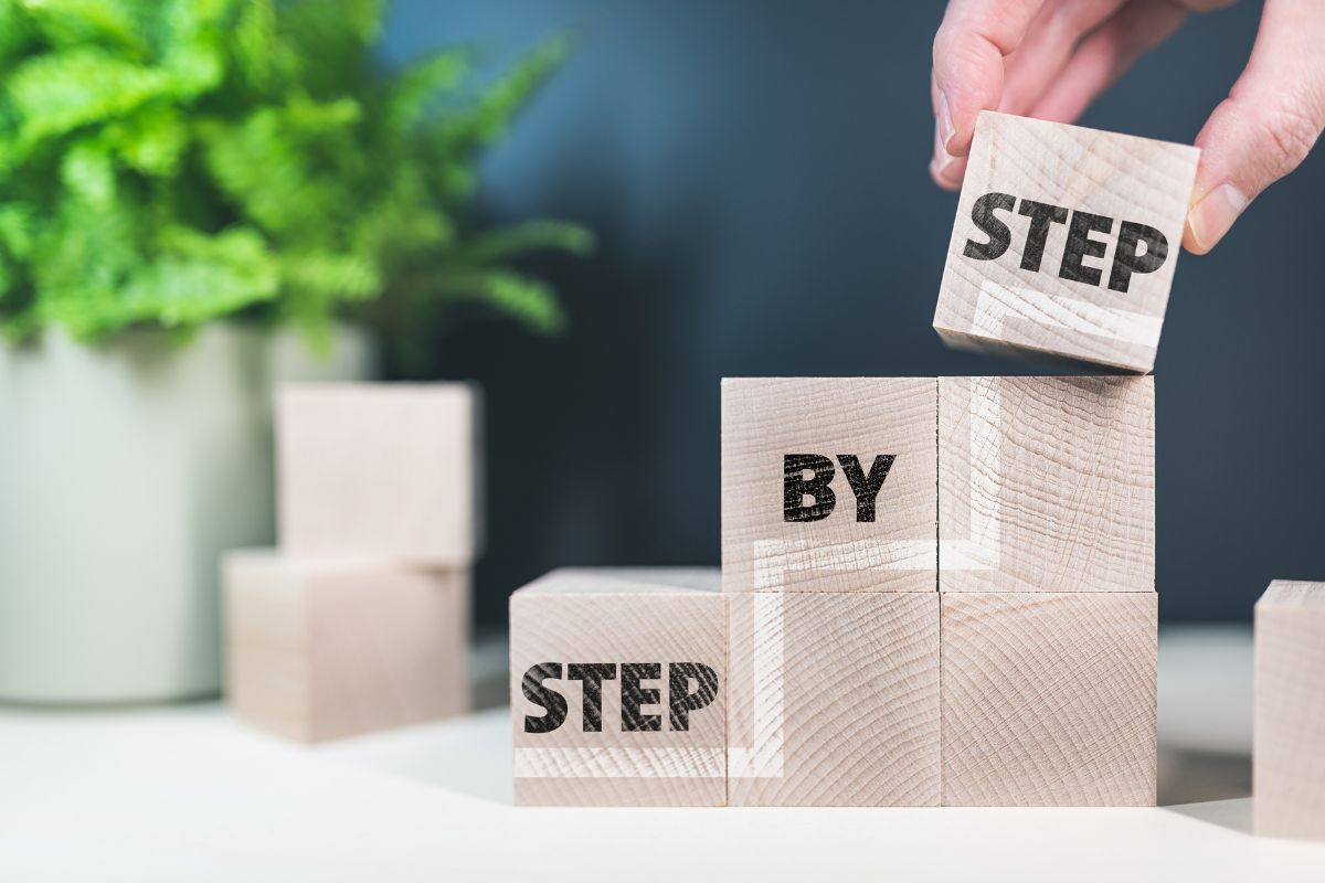 The photo tells about a plant, wooden cubes, with notes, and a man's hand putting the last cube indicating to take these steps to keep your money last and grow over time.