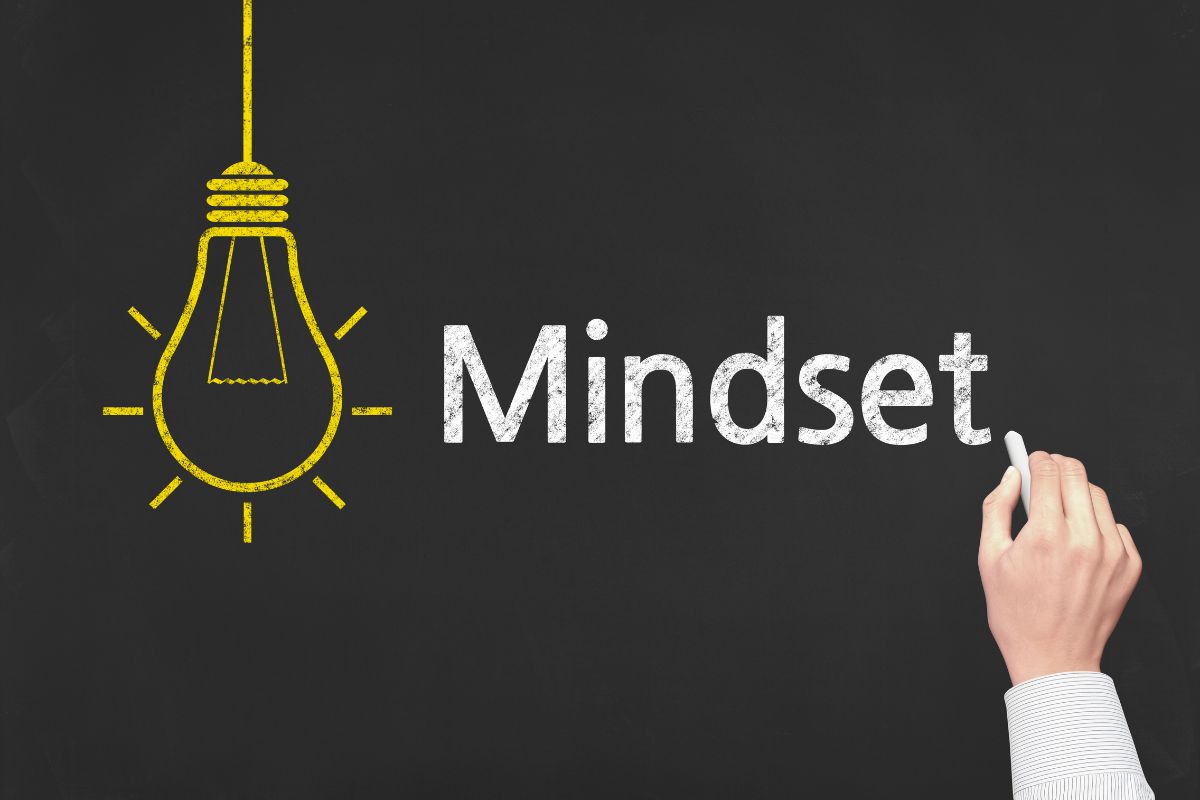 The photo tells about a board with a bulb drawing and a man's hand and writing on the board which refers to adopting a long-term mindset that helps with money motivation and builds lasting financial stability.