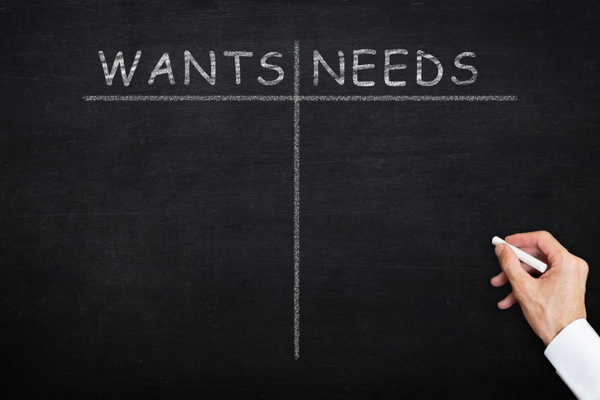 The picture tells about a man's hand and writing on the board which means prioritizing needs over wants is a smart step toward financial freedom.