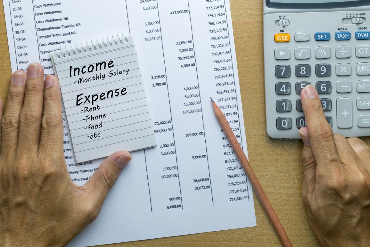 The picture shows papers with notes and numbers, a pen, a mini notebook with notes, and a man's hand calculating referring to track all income and expenses helps shows you where to cut back and plan better.
