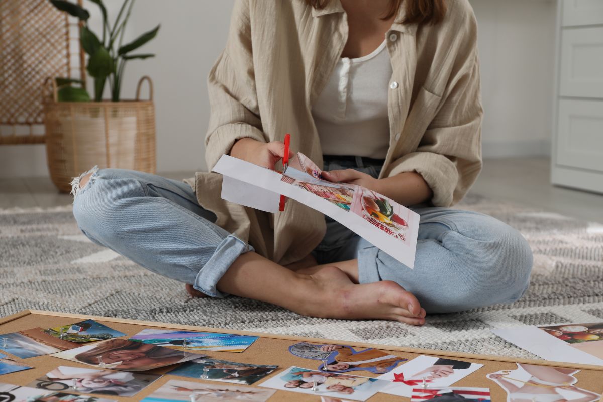 The photo tells about a board with pictures and a girl cutting the images referring to how creating your vision board makes it easier to stick to financial plans and make smarter money choices.