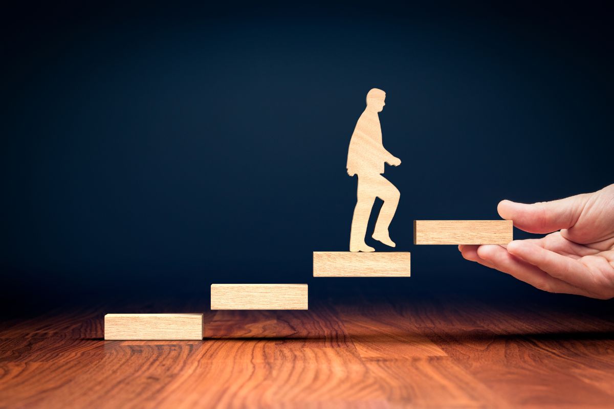The image tells about rectangular wooden, a human figure, and a man's hand holding a wooden rectangle which means investing in personal growth is a smart way to support financial goals.