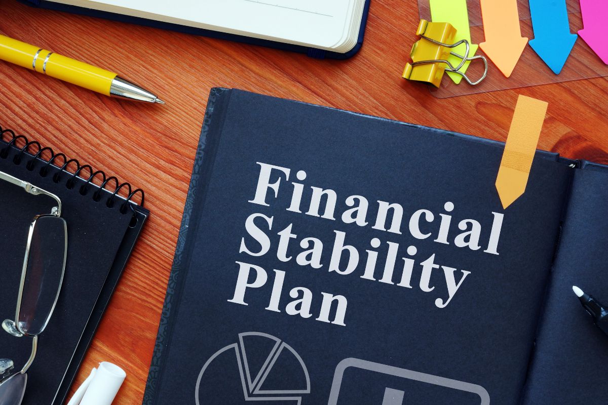 The image shows arrow papers, a notebook, a pen, an eyeglass, and a black notebook with notes indicating to time to become financially stable to improve your financial situation. 