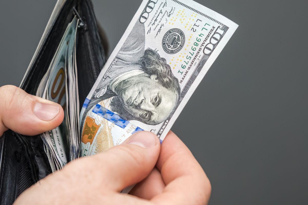 The image shows a man's hand holding a wallet with dollar bills referring to a no-spend challenge day that helps you reset your habits and a smart step towards financial freedom.